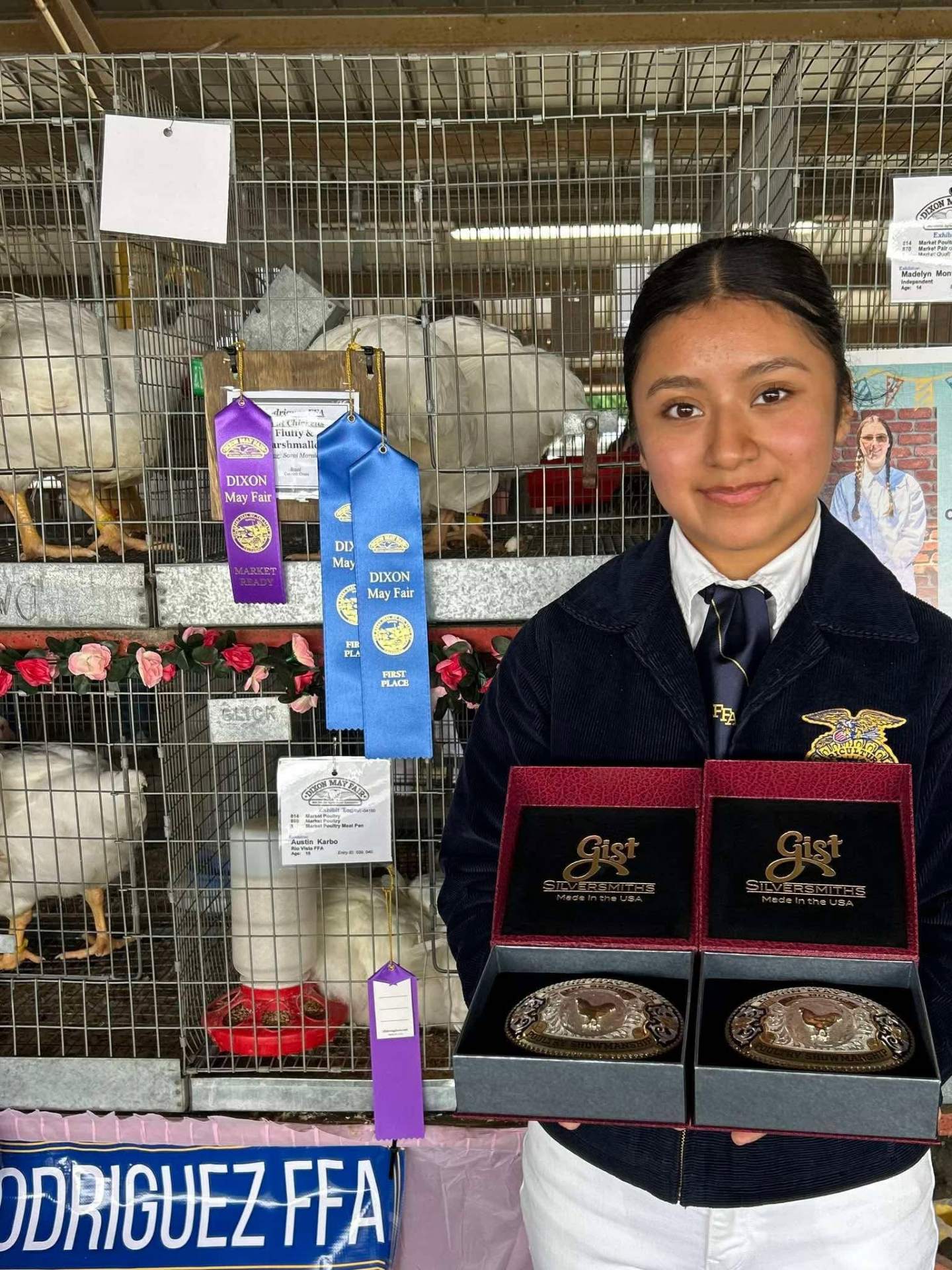 Young FFA exhibitor holding championship belt buckles beside her poultry ribbons at the Dixon May Fair
